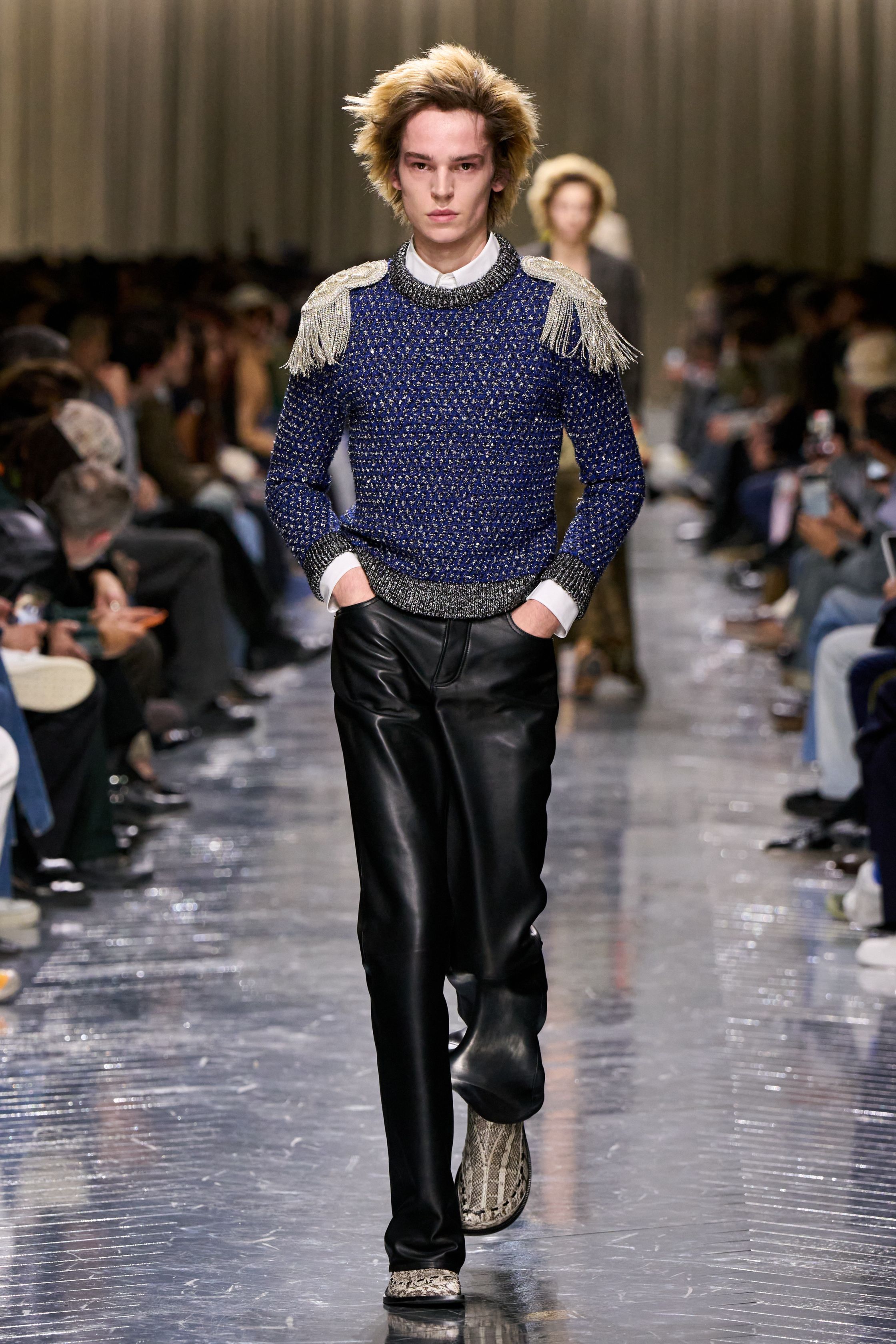 本季 Dior Men 2026 秋冬在克制与叛逆之间建立起新的男性气质坐标。轮廓上，柔软针织、披风式外套与军装结构形成张力对照，模糊正装与休闲、性别与功能的边界；材质层面，羊毛、皮革、毛绒与轻量技术面料并置，强化“触感叙事”。色彩从学院派的灰蓝、橄榄绿过渡至点状印花与手工肌理，传递一种被精心编排的随性。整体呈现出一种“新贵游牧者”形象：既有高级定制的工艺根基，又拥抱当代青年对自由、混搭与身份流动性的渴望-顽石频道趋势研究